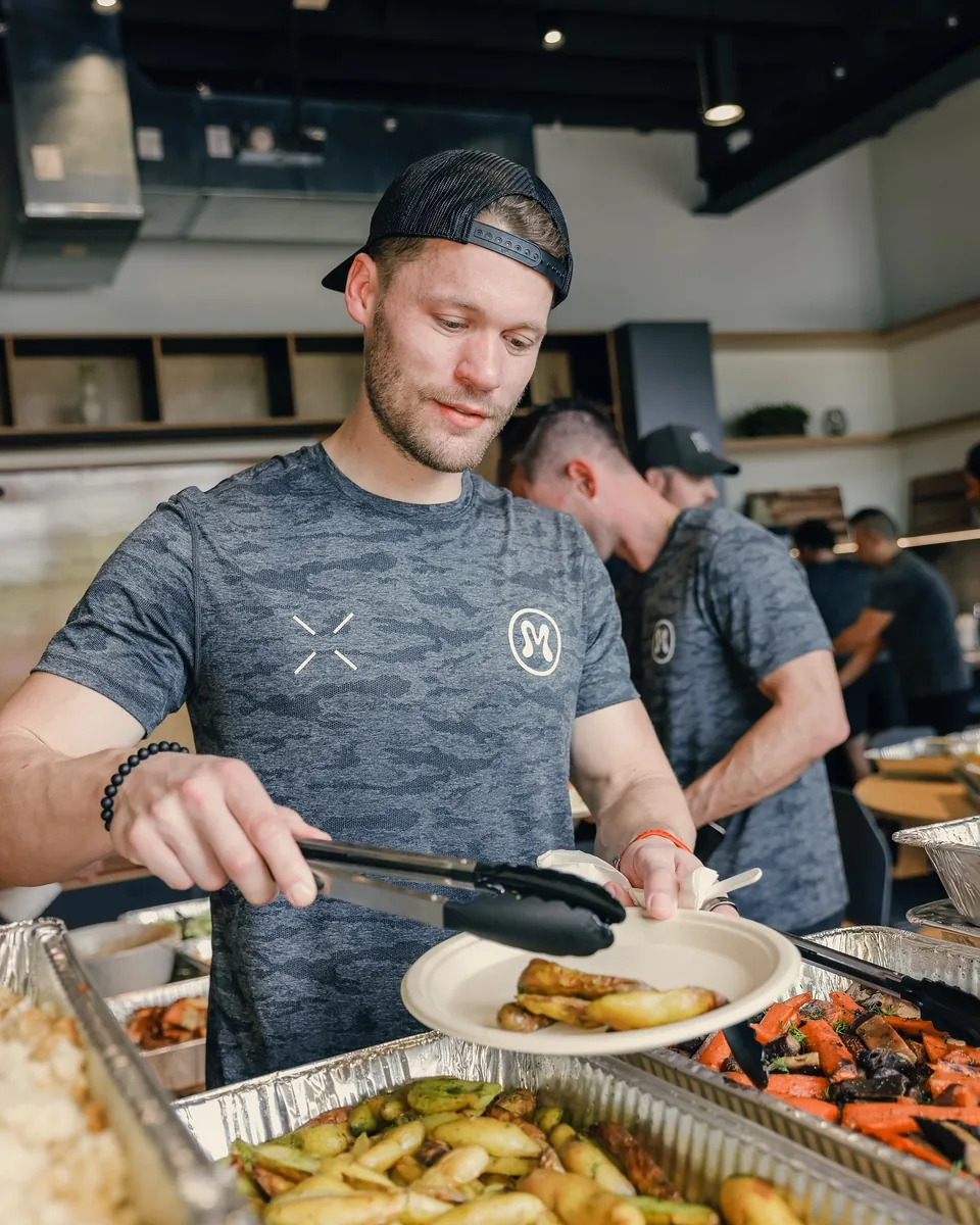 A colleague serving roasted vegetables from a workplace lunch spread