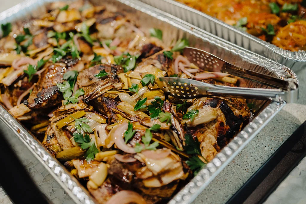 A catering tray of sliced steak and roasted onions ready for a shared lunch