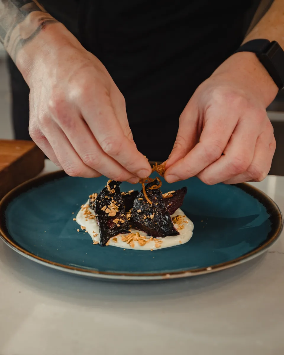 Chef plating roasted vegetables over a cream base